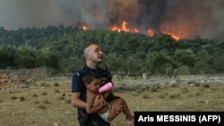 Un polițist grec evacuează un copil dintr-un incendiu de vegetație în satul Agios Charamlabos, în apropiere de capitala Atena, pe 18 iulie 2023.