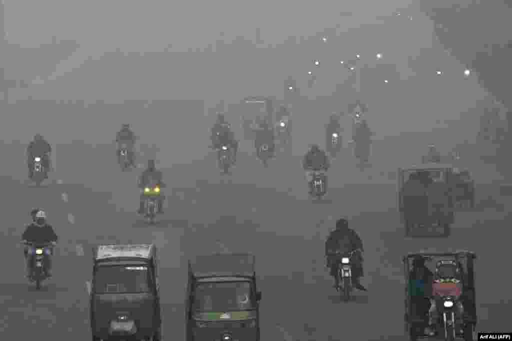 Navetiștii își croiesc drumul pe o stradă în mijlocul smogului dens din Lahore, Pakistan.