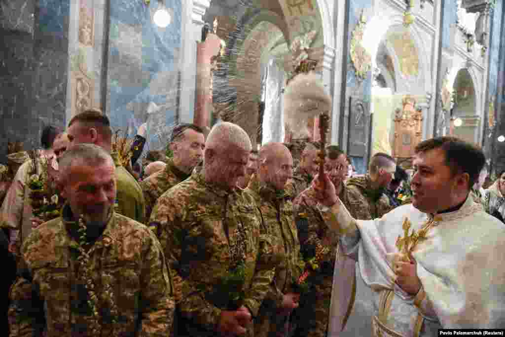 Украинските војници се прскаат со света вода додека присуствуваат на осветувањето на гранките од врба на Цветници во црквата во Лвив на 17 април.