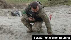 Украин аскери жарылбай калган кассеталык бомбанын бөлүктөрүн жыйнап жатат.