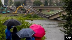 Oamenii urmăresc de la distanță, sub umbrele, la Dresda lucrările de scoatere din Elba a porțiunii căzute din Podul Carola, la 13 septembrie.