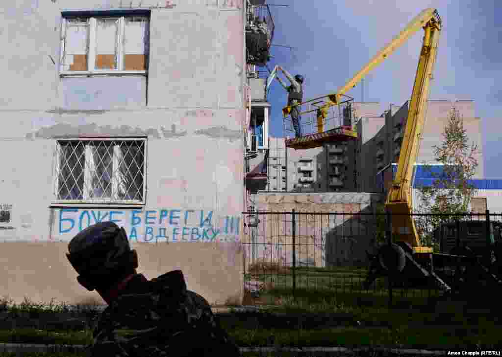 Пока ван Хелтен поднимается на рабочее место, украинский военный проходит мимо граффити: “Боже, береги Авдеевку”.