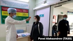 Медработник замеряет температуру тела посетителя в больнице.