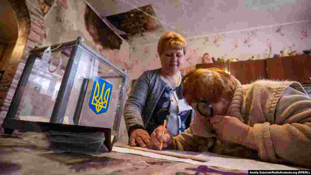 Жінка голосує у своєму будинку, у який було пряме влучення артилерійського снаряда. Деякі з будинків відновлені лише частково. 
