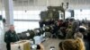 Ракета 9М729, схована в пусковому контейнері, на тлі пускової установки комплексу «Іскандер», для якого вона призначена, на виставці-брифінгу під Москвою, січень 2019 року