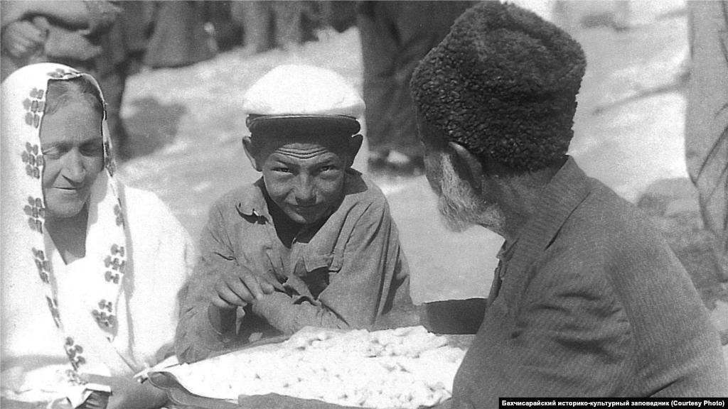 Вуличний торговець. Бахчисарай, 1920-ті. Більшість ремісників самі продавали виготовлений ними товар у власних крамницях, але кримське місто неможливо уявити без базару. Існувала і розносна торгівля &ndash; коробейники, обвішані намистами, ланцюжками, сукнями, чубуками й іншими предметами, ходили міськими вулицями